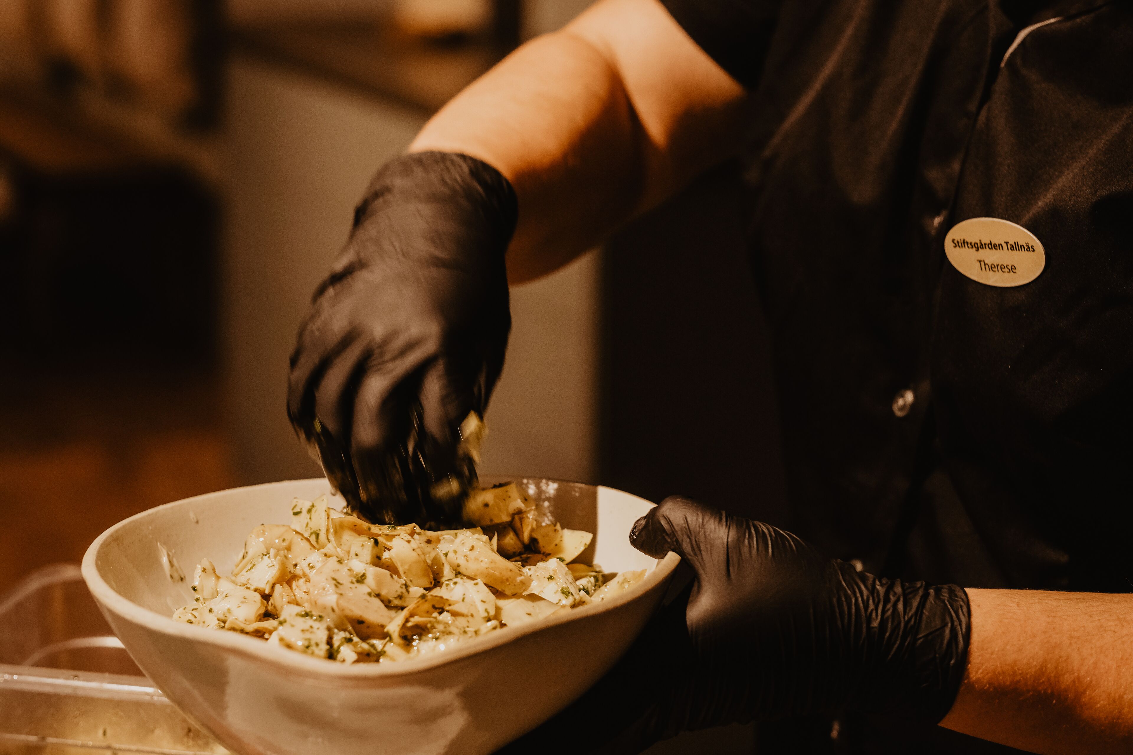 A person in a black uniform with a name tag, preparing food in a bowl.