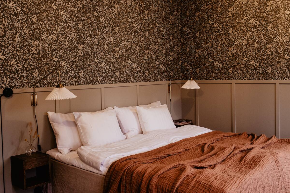 A neatly made bed with white linens and a brown blanket, flanked by two bedside lamps.
