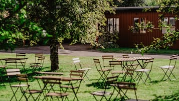 A grassy outdoor area with folding tables and chairs, a tree, and a wooden building in the background.