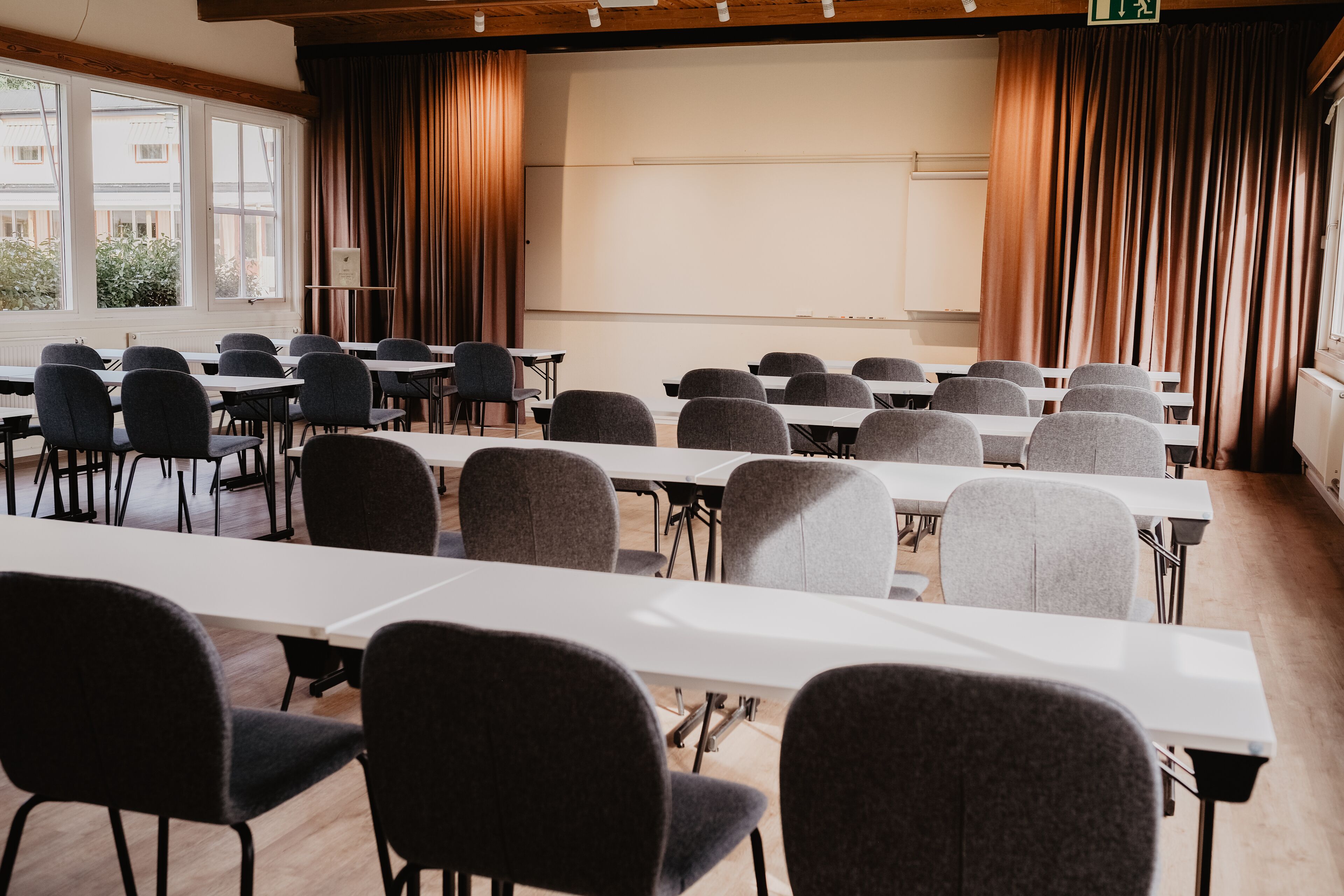 Un salón de conferencias con largas mesas y sillas, ventanas amplias y cortinas.