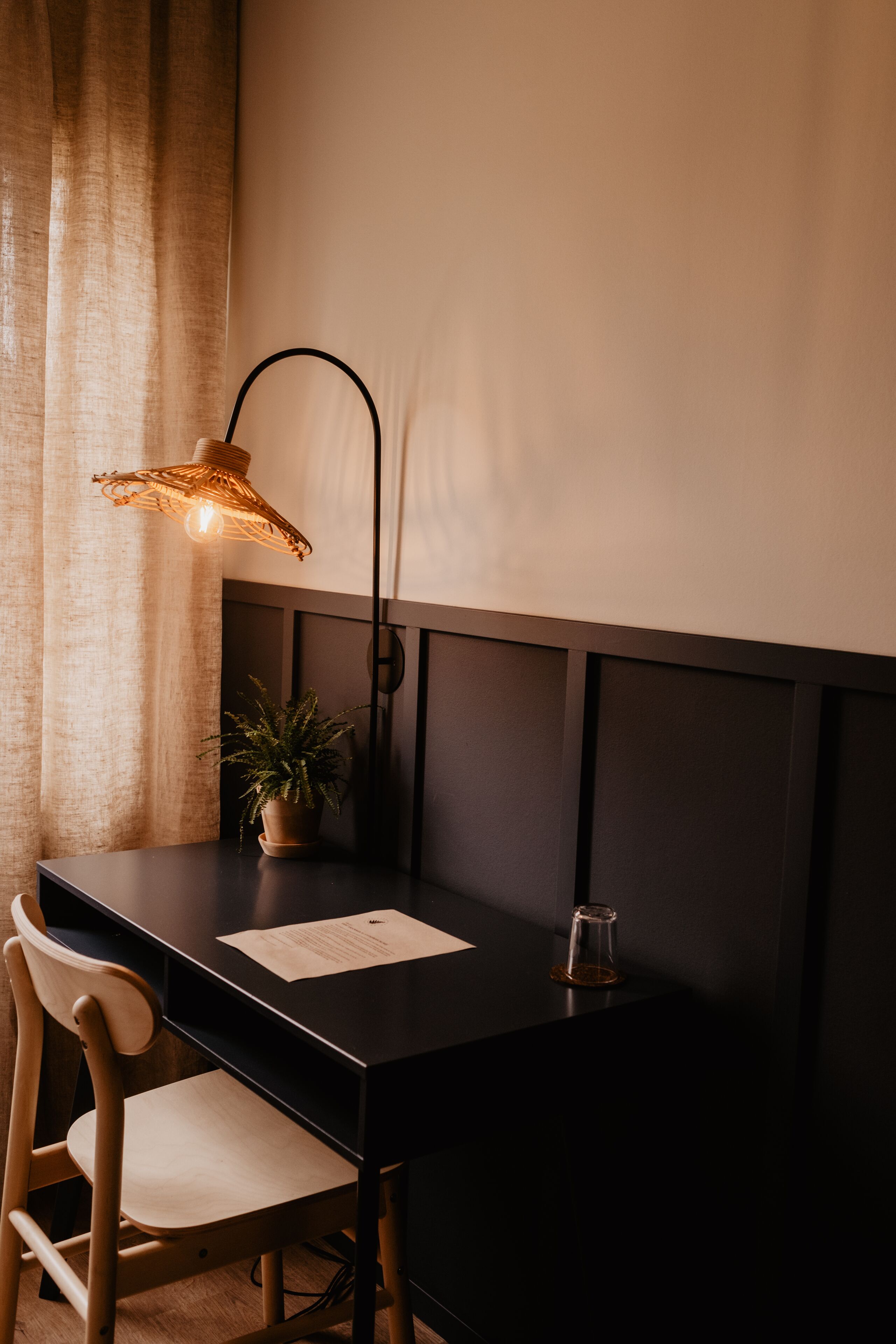 Un escritorio de madera oscura con una silla, una planta en maceta, una lámpara y un vaso de agua.
