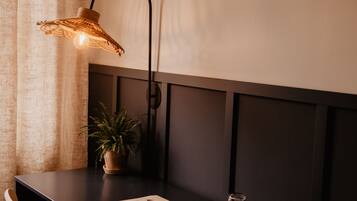 Un escritorio de madera oscura con una silla, una planta en maceta, una lámpara y un vaso de agua.