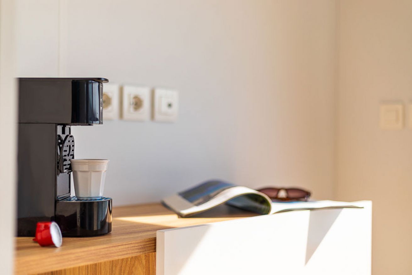 Una cafetera con una taza y un libro sobre una superficie de madera.