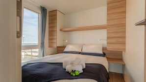 Une chambre d’hôtel moderne avec un grand lit, une tête de lit en bois et une vue sur la plage, visible à travers une grande fenêtre.