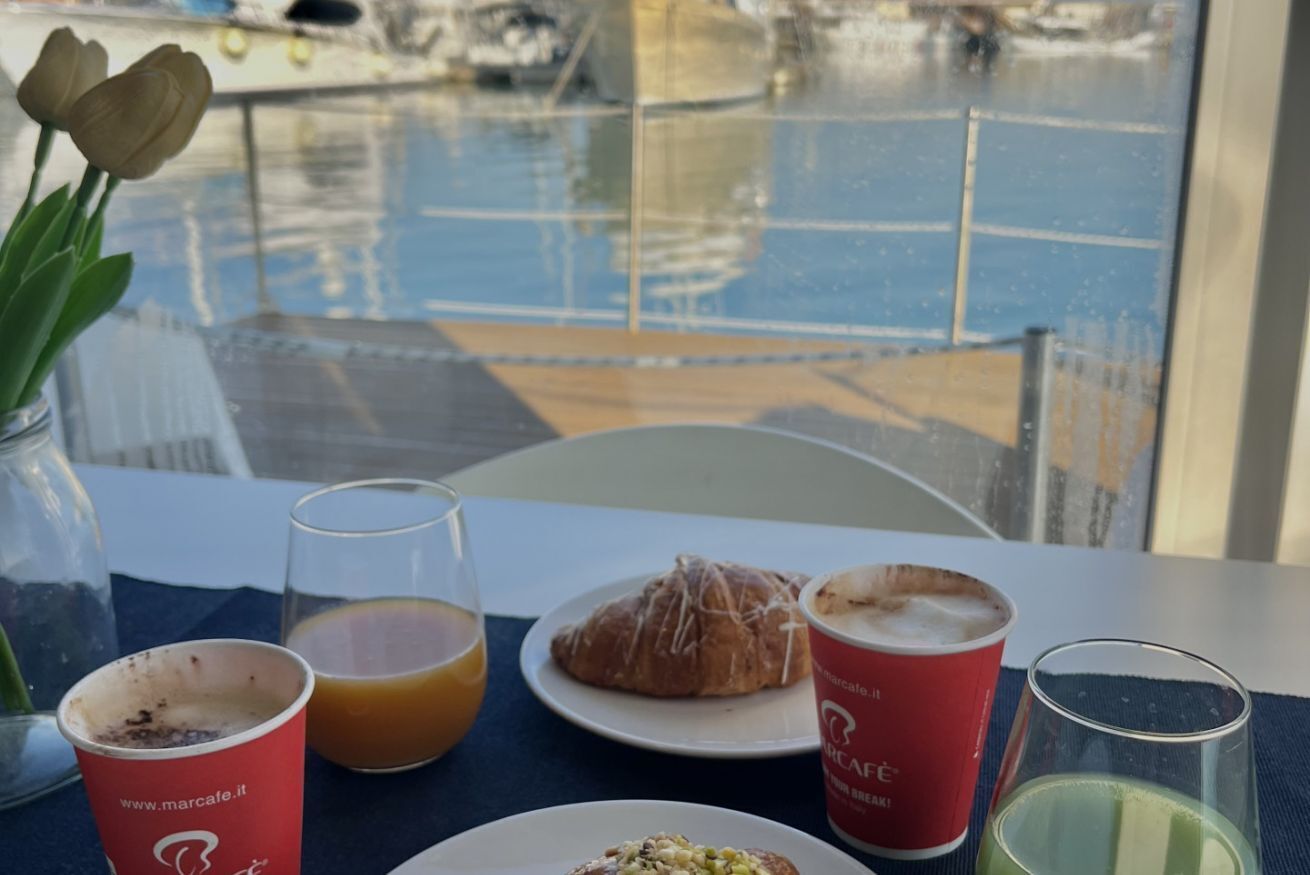 Una mesa con un croissant, un vaso de jugo de naranja, una taza de café y un vaso de jugo verde.