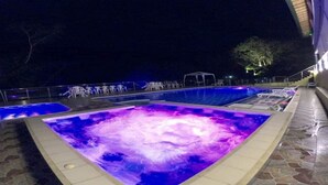 Un espace piscine comprenant plusieurs bassins, dont un jacuzzi, entouré de chaises longues et doté d’un espace de repos abrité.