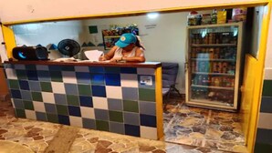 Un comptoir d’enregistrement avec un mur recouvert de carreaux, un ventilateur et un réfrigérateur rempli de boissons.