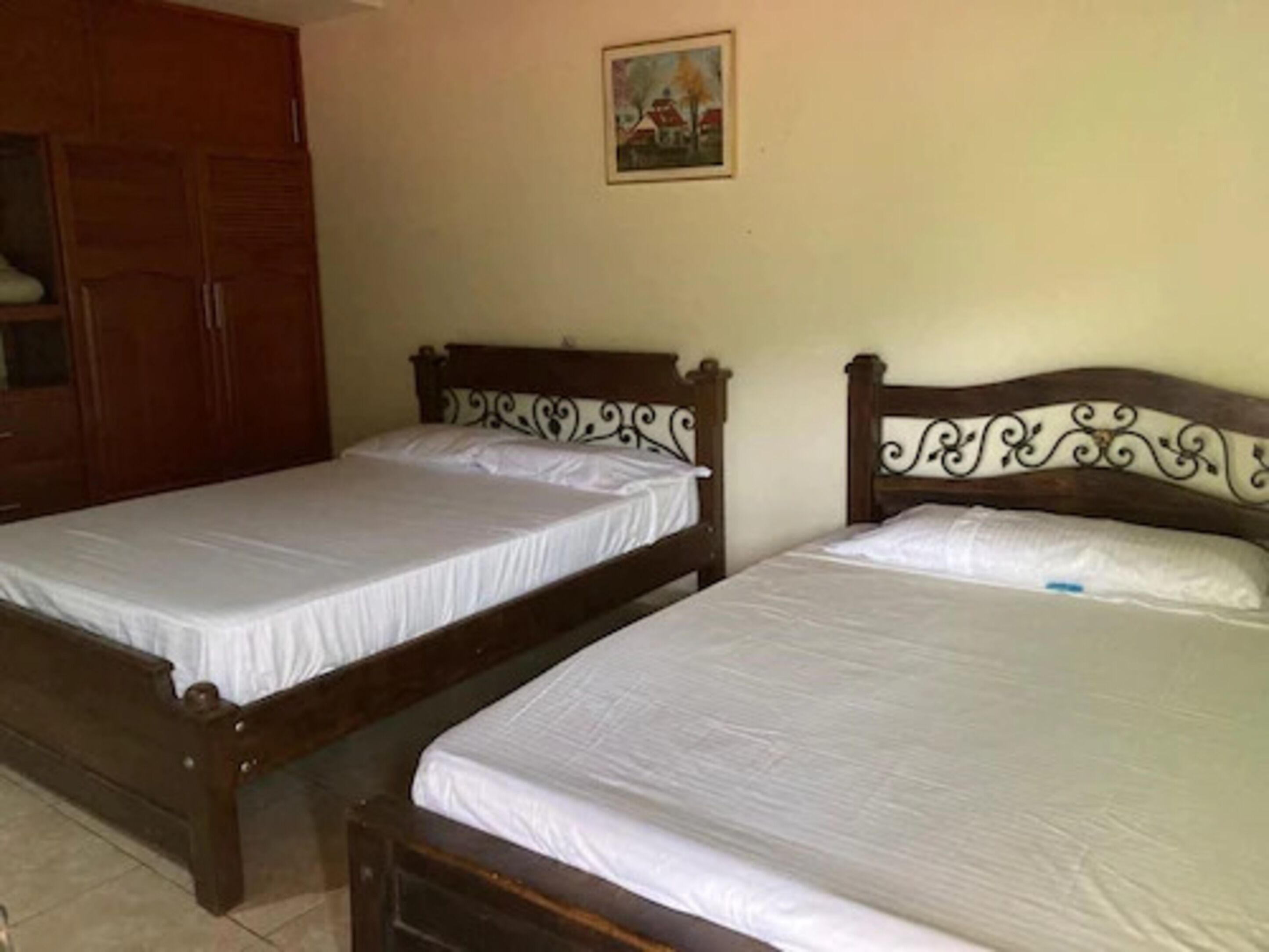 Dos camas de madera con sábanas blancas en una habitación con un armario de madera y un cuadro en la pared.