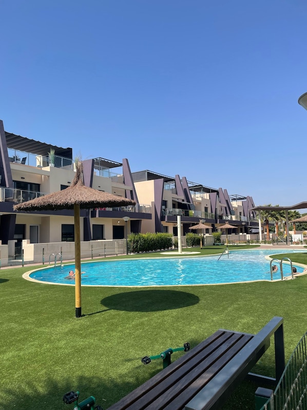 A swimming pool surrounded by a well-maintained lawn, with modern buildings in the background.