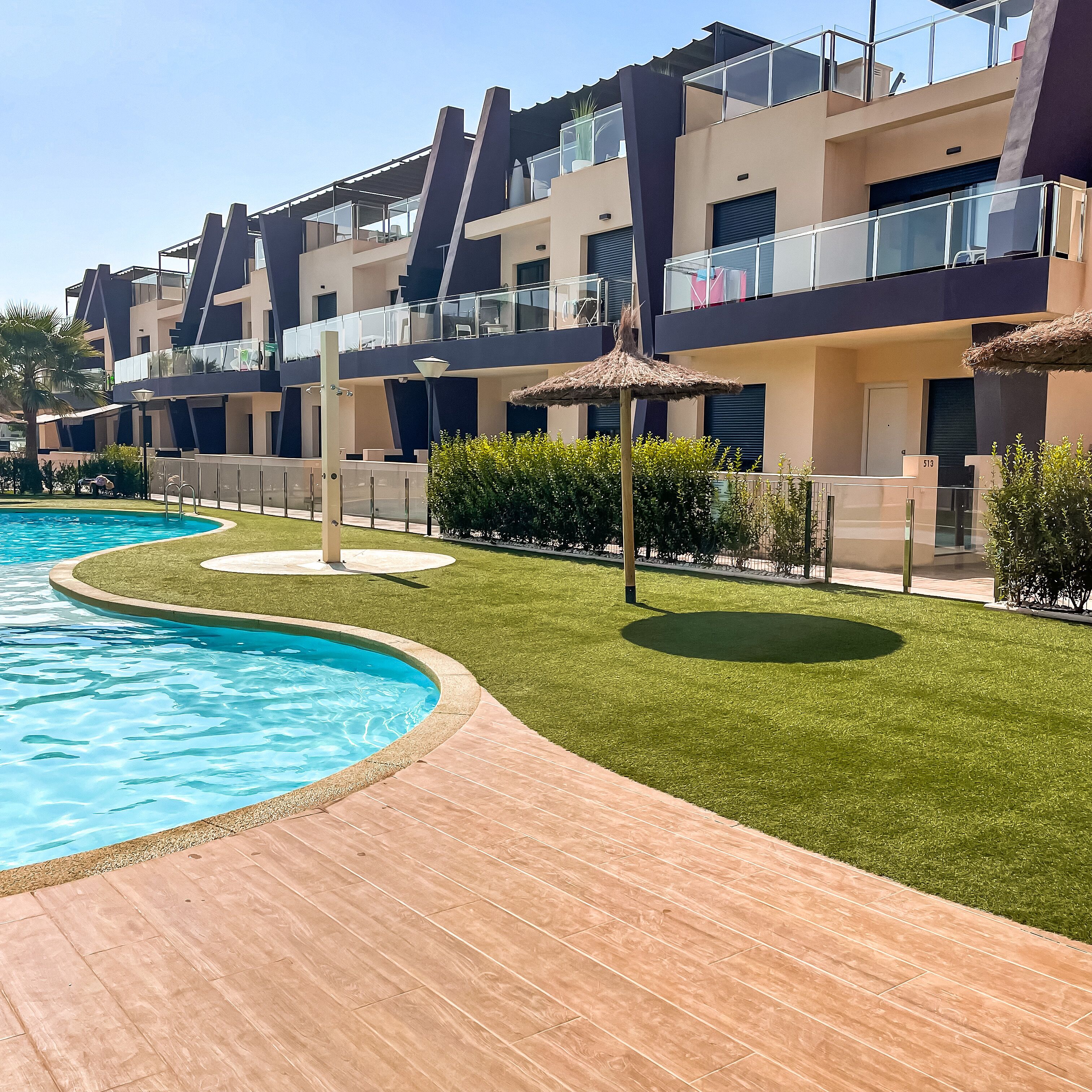 A modern hotel with a swimming pool, outdoor lounge area, and well-maintained lawn.