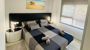 Un dormitorio moderno con una cama grande, una mesita de noche, una lámpara de pared y un cuadro con motivos playeros.