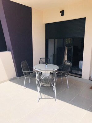 A modern outdoor patio with a round table and four chairs, a potted plant, and a sliding glass door leading to a balcony.