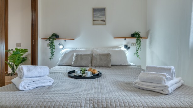 Una cama bien hecha con una bandeja de desayuno, toallas y una pequeña planta.
