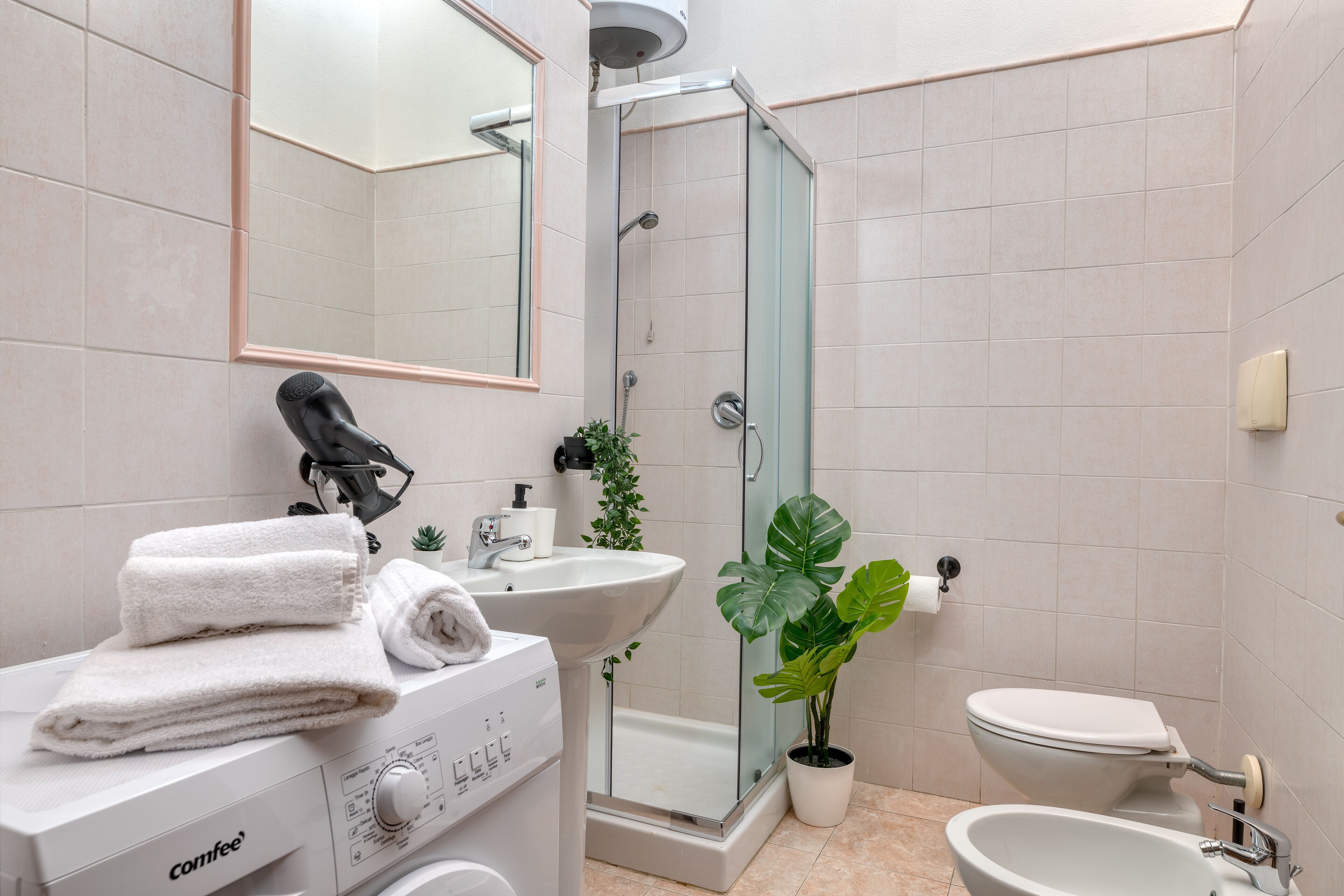 A modern bathroom with a washing machine, a sink, a toilet, and a glass-enclosed shower.