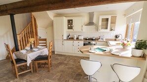 A kitchen with white cabinets, a wooden staircase, and a dining area with two bar stools.