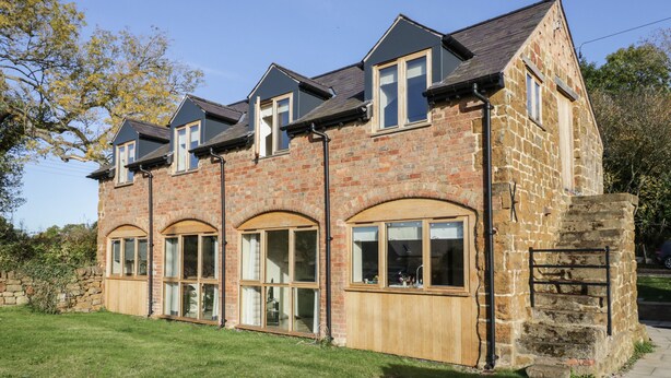 A two-story stone building with a pitched roof, large windows, and a stone staircase leading to the entrance.