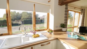 A kitchen with a large window, wooden countertop, and a bowl of fruit on the counter.