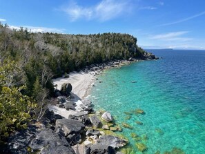 Rannikkomaisema, jossa on kirkas turkoosinvärinen vesi, hiekkaranta ja metsäinen rinnemäki.