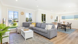 A spacious living room with a grey sectional sofa, a white coffee table, and a dining area with a wooden table and chairs.