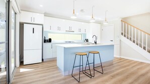 A modern kitchen with white cabinets, a central island with stools, a built-in oven, and a stainless steel sink.