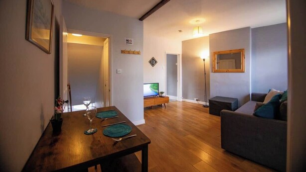 A dining area with a wooden table, two chairs, and a television in the background. - George's City Centre Apartment - Salisbury (Salisbury)
