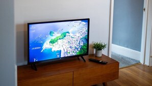 A television on a wooden stand, a remote control, and a small potted plant on a white wall. - George's City Centre Apartment - Salisbury (Salisbury)