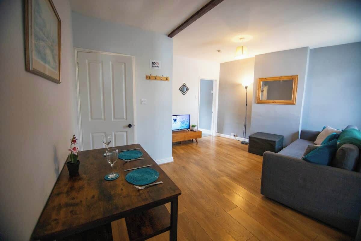 Una sala de estar con un sofá, una mesa de comedor con individuales, un televisor y una lámpara de pie.