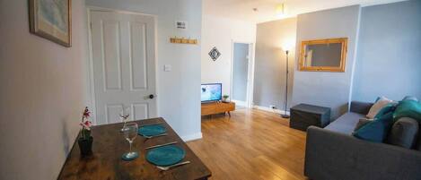 Una sala de estar con un sofá, una mesa de comedor con individuales, un televisor y una lámpara de pie.