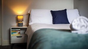 Ein Hotelzimmer mit einem Bett, einer Nachttischlampe, einem Nachttisch mit Büchern und einer Wandleuchte.
