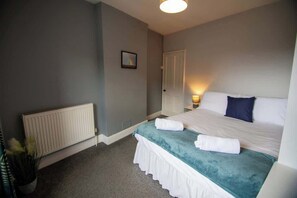 Habitación de hotel con cama, radiador, mesita de noche y un cuadro colgado en la pared.
