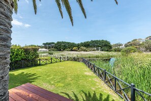 Zona verde y bien cuidada con un muelle de madera, rodeada por una valla metálica y una masa de agua.