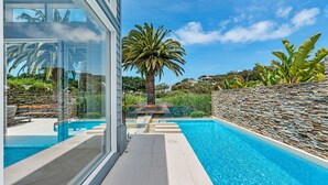 Une piscine moderne avec un mur en pierre et des palmiers en arrière-plan.
