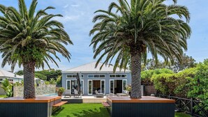 Une maison moderne dotée d’une pelouse bien entretenue, de deux palmiers et d’un patio aménagé avec du mobilier d’extérieur.