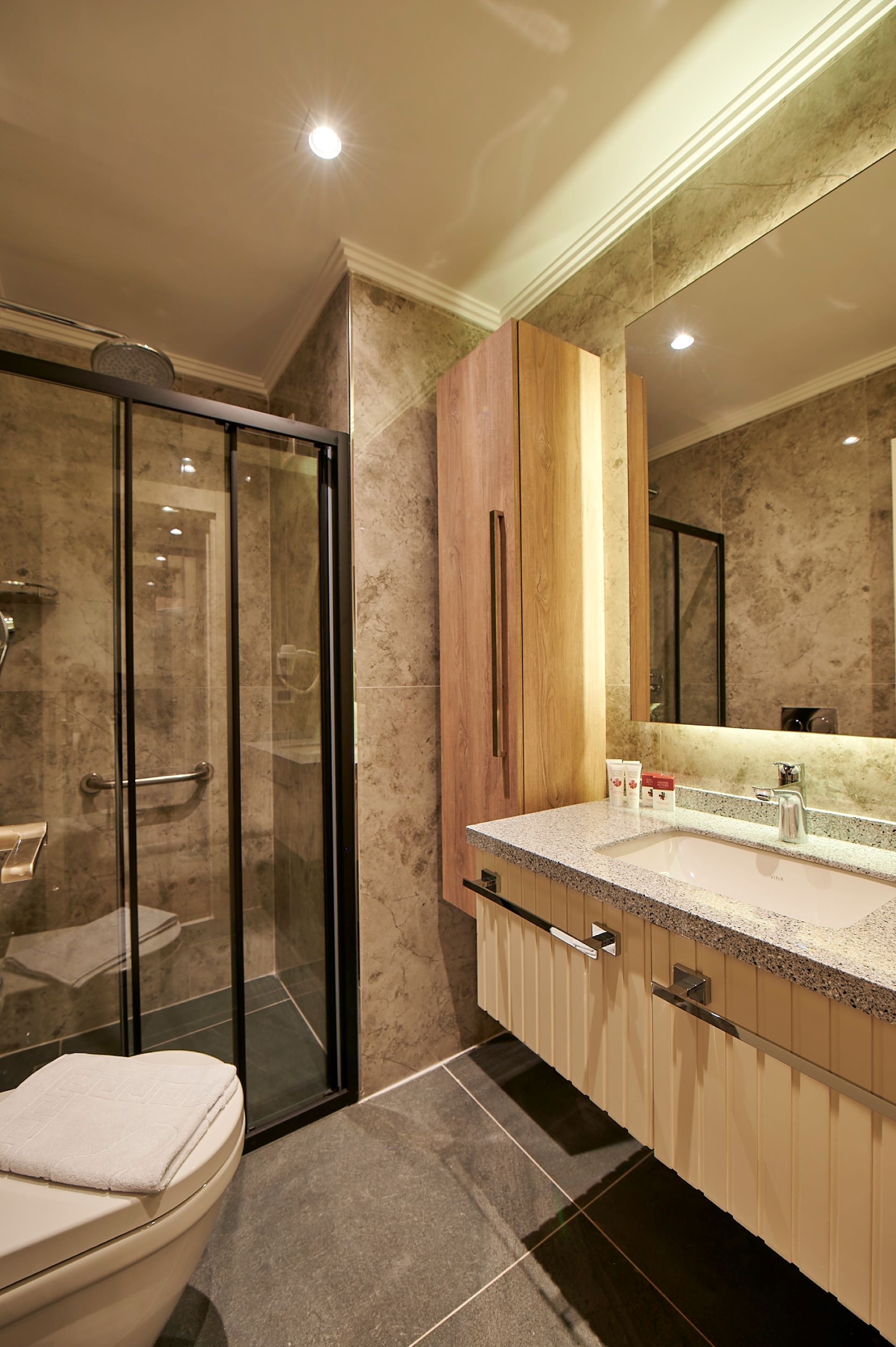 Un baño moderno con cabina de ducha de vidrio, un espejo grande y suelo de baldosas de mármol.