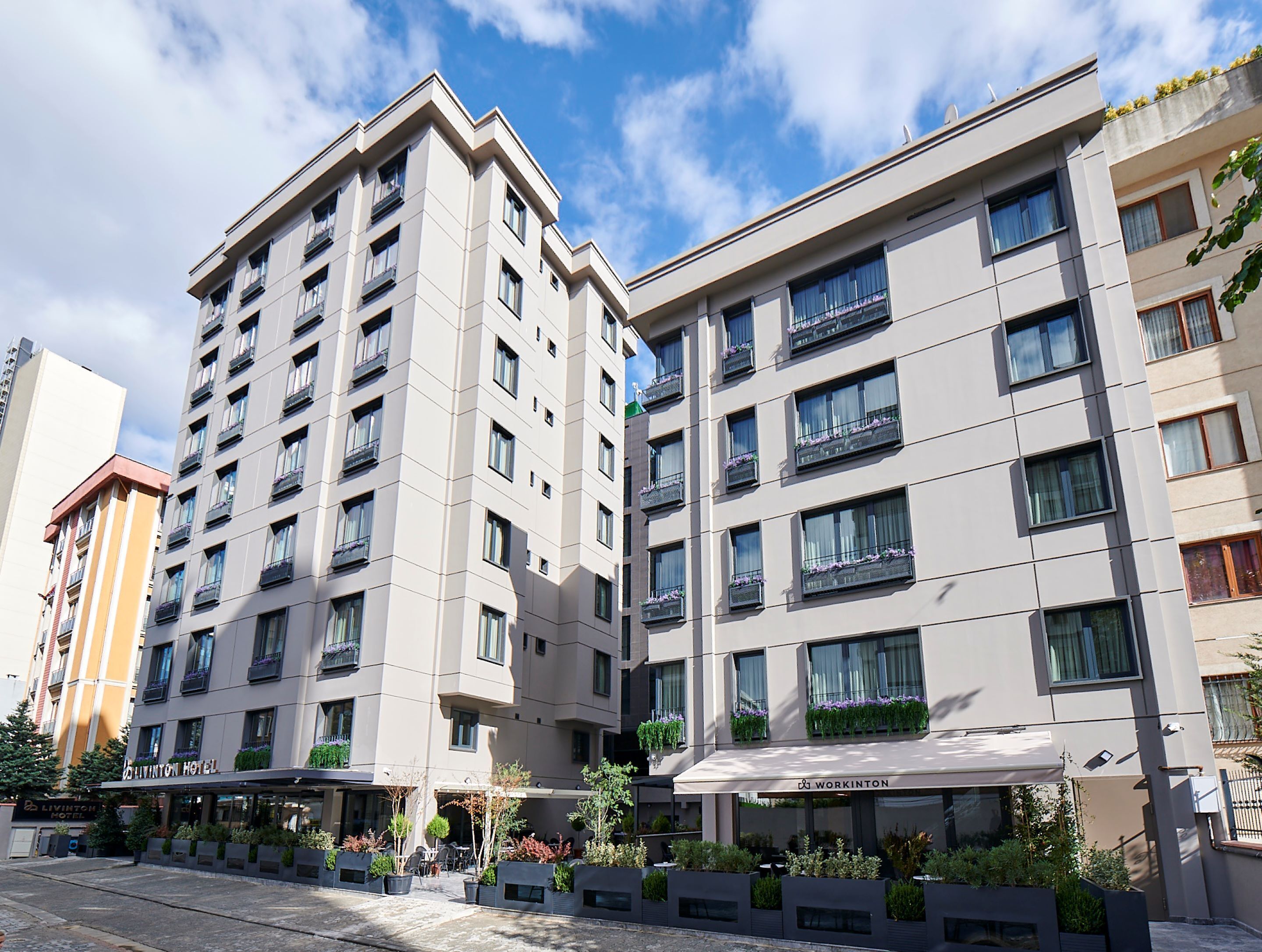A modern hotel building with multiple floors, balconies with plants, and a clear sky.