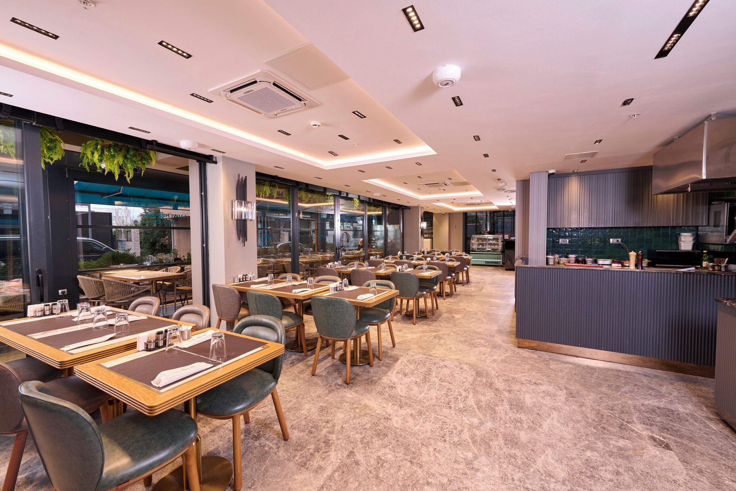 Un interior de restaurante moderno con varias mesas, sillas y una zona de cocina.