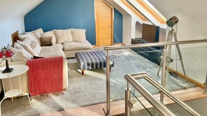 A modern loft bedroom with a blue accent wall, a sofa, a small table, and a red throw blanket.