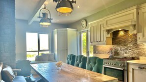 A modern kitchen with a stone backsplash, a built-in oven, and a dining area with a wooden table and green upholstered chairs.