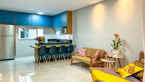 Une cuisine moderne avec des meubles de couleur bleue, un coin repas avec des chaises, un canapé et une petite table agrémentée d’une plante.