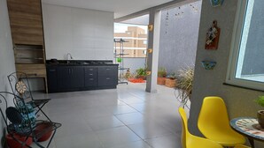 Une cuisine moderne avec des meubles de couleur sombre, un coin repas avec des chaises jaunes et une vue sur un bâtiment en arrière-plan.