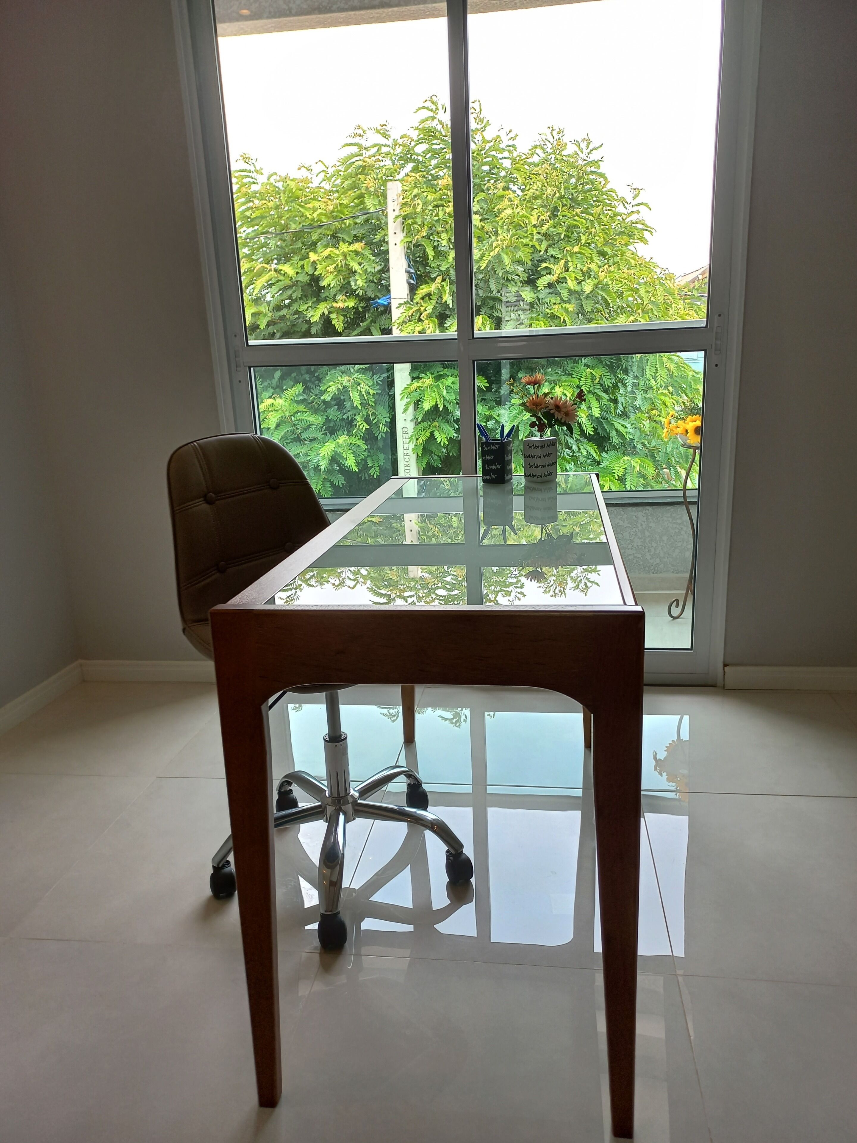 Une pièce avec une table à plateau en verre, une chaise marron et une vue sur la verdure à l’extérieur.