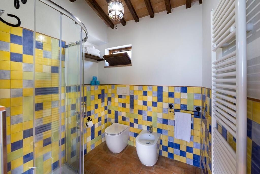 Un baño con ducha, inodoro y bidé, con azulejos amarillos y azules.