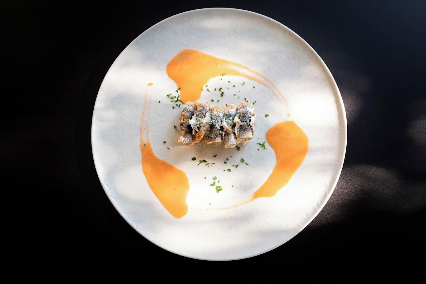 Un piatto con un alimento, forse del pesce, guarnito con erbe aromatiche e accompagnato da una salsa.