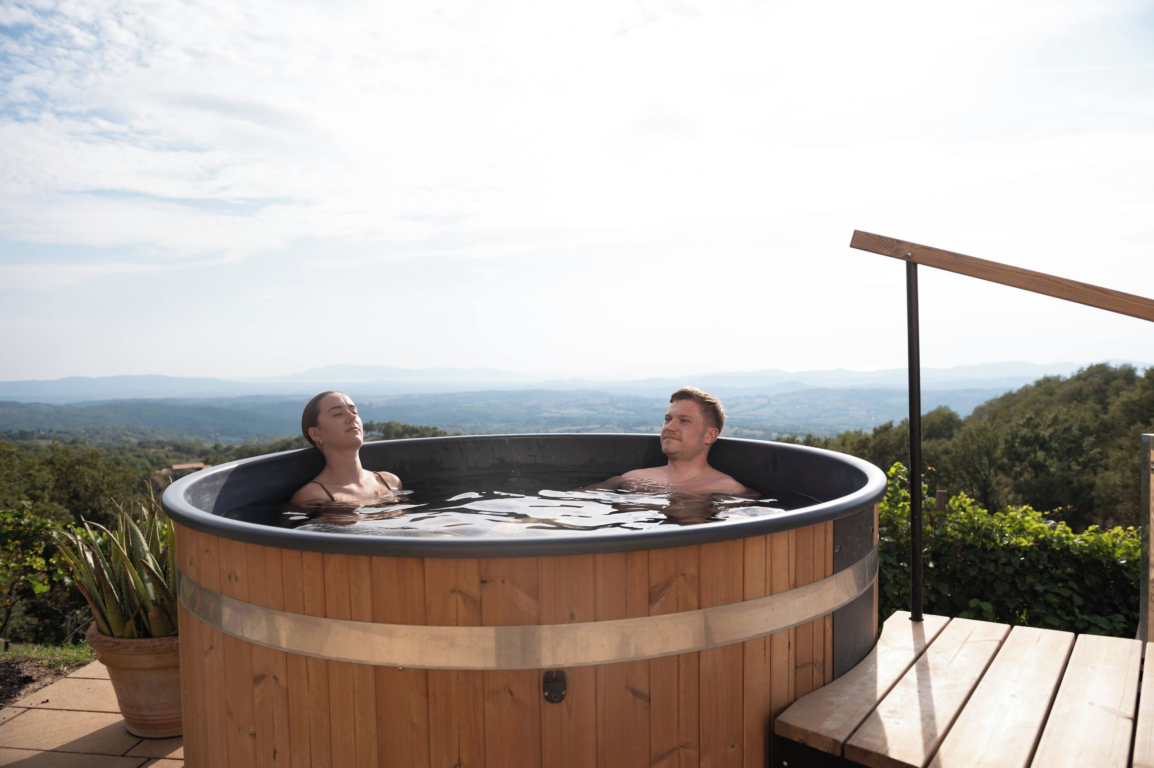 Due persone in una vasca idromassaggio in legno con una vista panoramica.