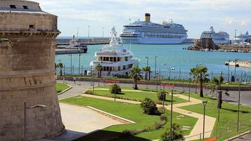 A coastal area with a historic tower, a marina with large cruise ships, and a well-maintained public square with pathways and greenery.
