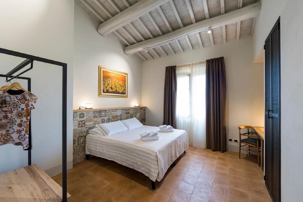 A bedroom with a bed, a wooden table, a chair, a hanging rack, and a painting on the wall.