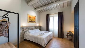 A bedroom with a bed, a wooden table, a chair, a hanging rack, and a painting on the wall.