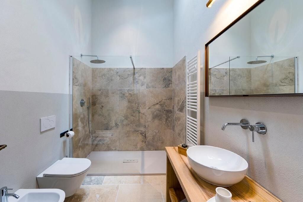A modern bathroom with a glass-enclosed shower, a white sink, and a toilet.