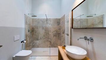 A modern bathroom with a glass-enclosed shower, a white sink, and a toilet.
