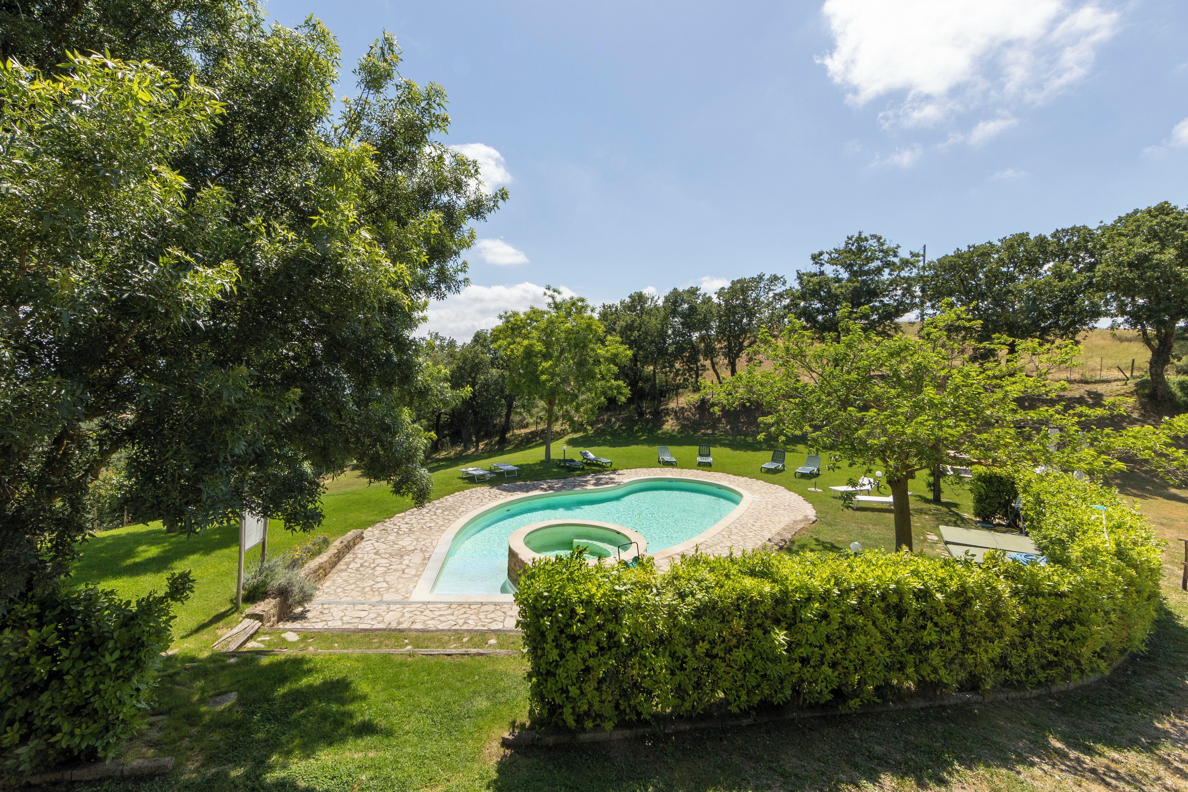 A swimming pool with a stone deck, surrounded by a well-maintained lawn and trees.